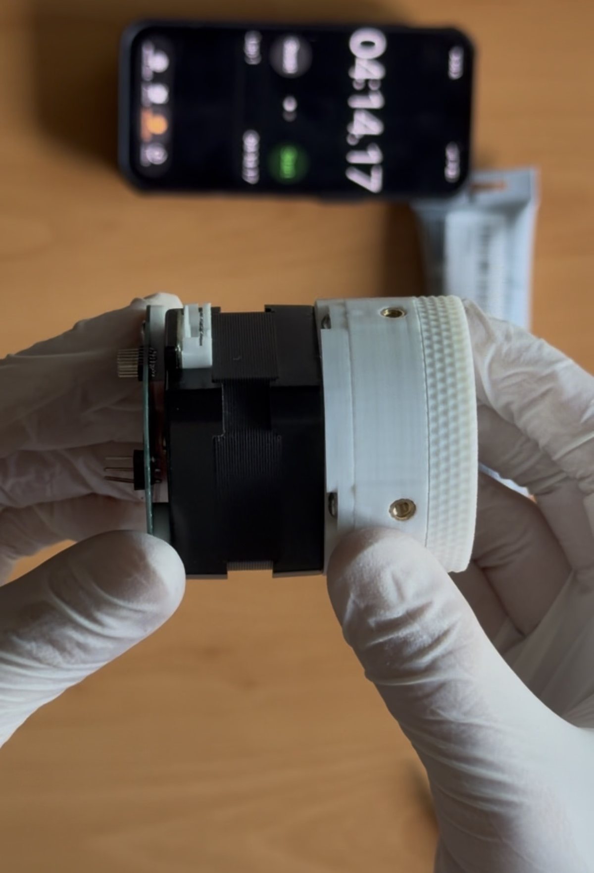 The assembled HDP30 held in gloved hands: a thin white printed gearbox with a knurled output ring, bolted to the face of a black NEMA 17 stepper.