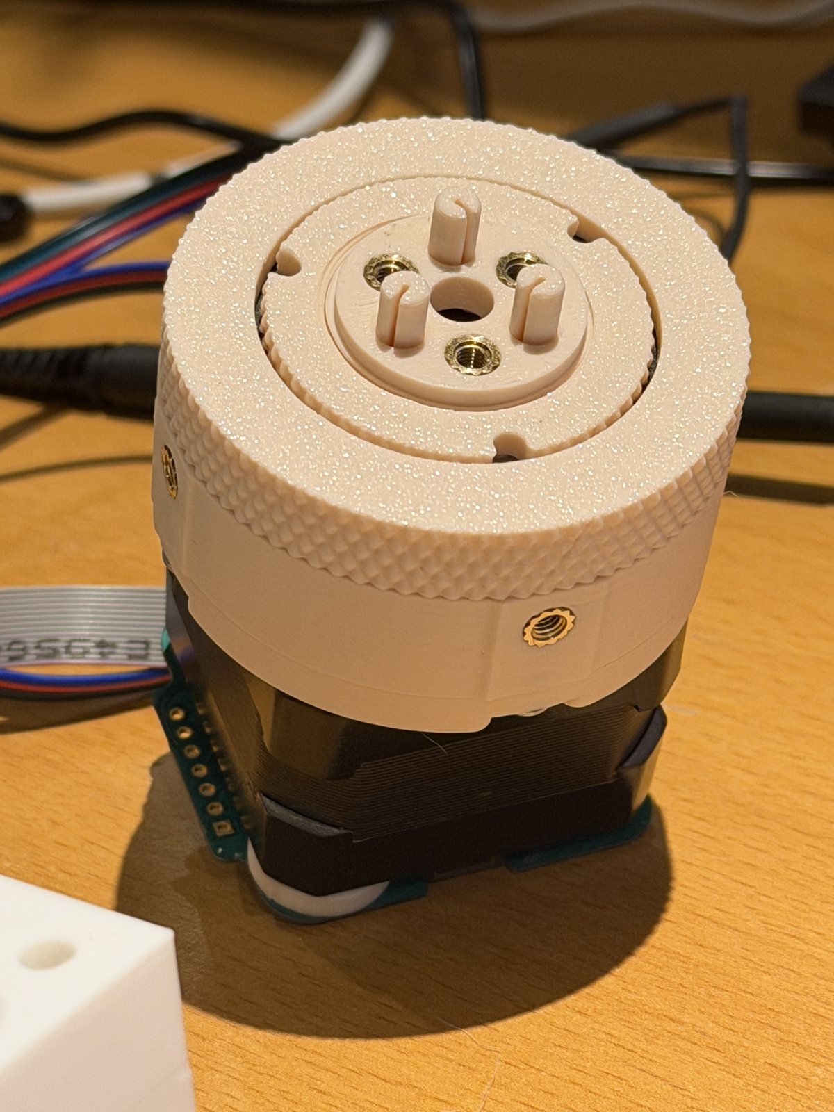 The assembled Rinnegan drive v2.0 on a NEMA 17 stepper: a cream printed gearbox with a knurled output ring, four brass inserts on the output face and three printed shear pins.